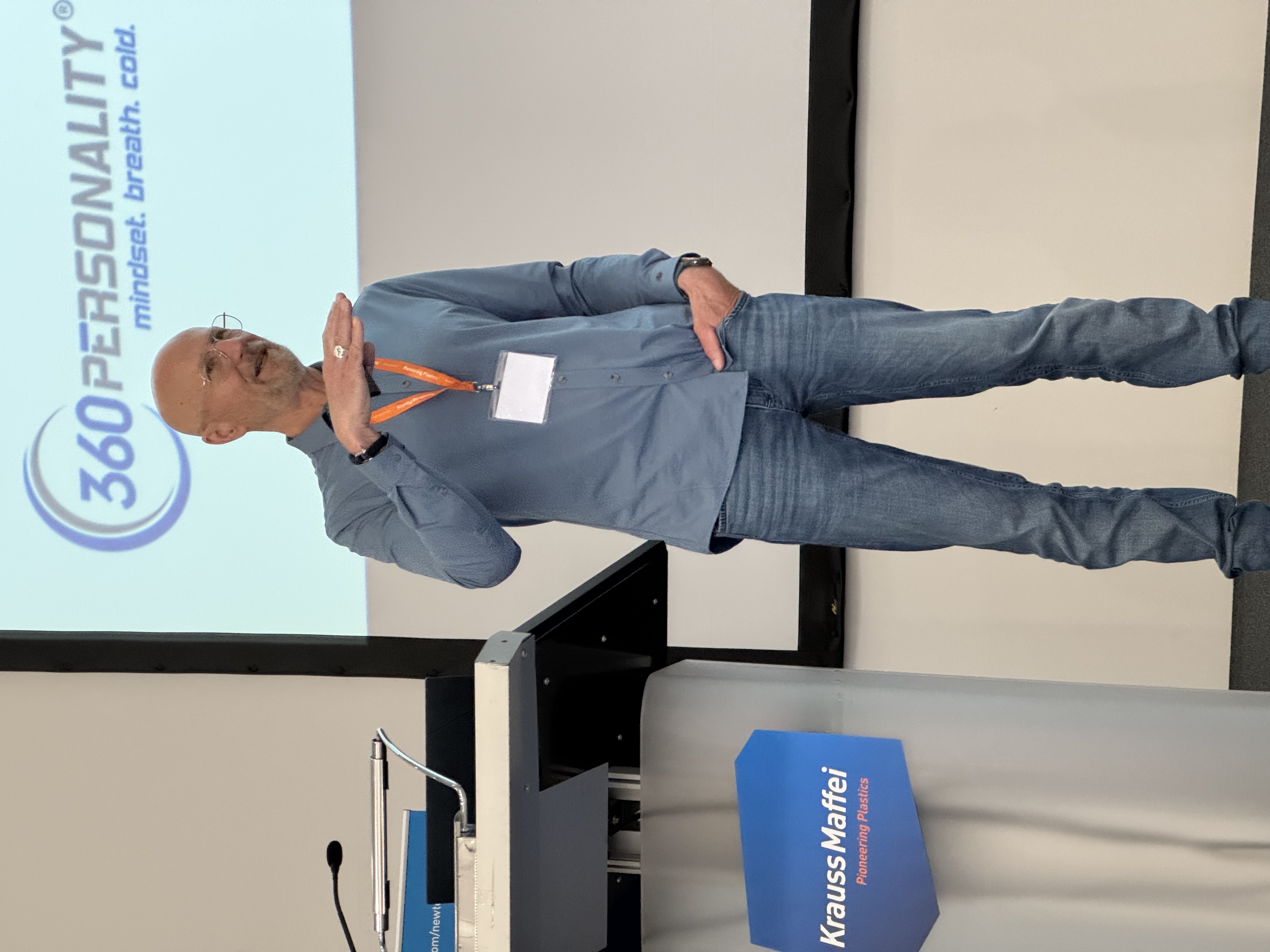 Elmar Büttner hält eine Keynote vor Publikum, im Hintergrund das Logo des Kunden